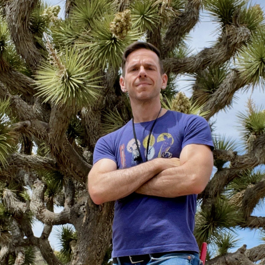 A man stands in front of a twisty, spiky desert plant with his arms crossed